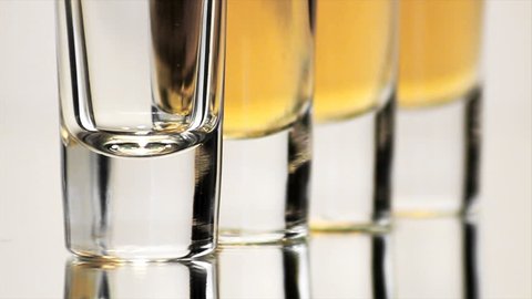 Four Shot Glasses Bottoms. Extreme close up (ECU) of the base of four double shot glasses as alcohol is poured into them, one by one.