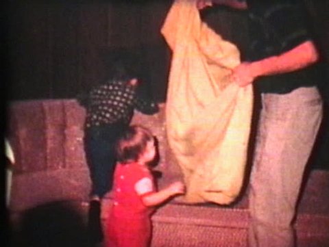 A little girl gets a crazy blanket ride from her daddy in the living room.