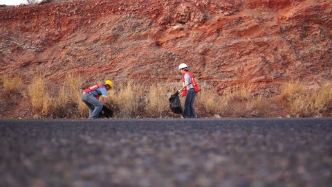 Low angle shot of a male and a female worker in safety gear cleaning up garbage on the side of the highway in an environmental clean up effort. Stockvideó