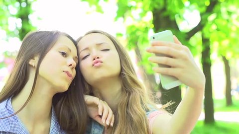 Outdoor portrait of teen friends taking photos with a smartphone. Two Teenager girlfriends having fun in a park. Teenage Girls making self portrait. Selfie. Slow motion 240 fps. Full HD 1080p 