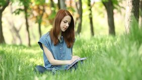 Young redhead smiling woman with notebook in the city park.