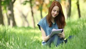 Young redhead smiling woman with notebook in the city park.