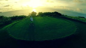 Flight over a beautiful golf course passing by a golfer teeing off and ending over the indian ocean with amazing sunset in background