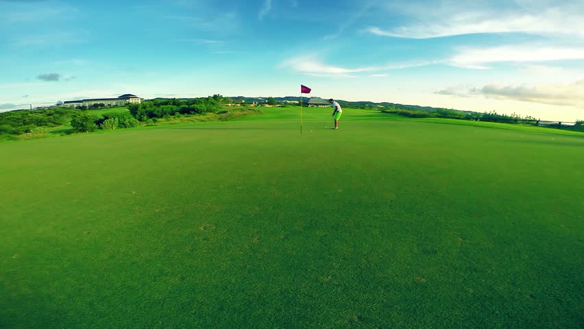 Wide angle shot of a beautiful golf course with golfer making his putt