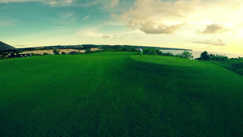 Aerial shot of a golfer teeing off on a beautiful golf course during sunset