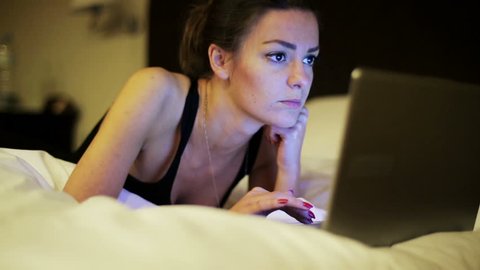 Woman lying on bed and working on laptop, steadycam shot.

