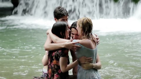 girls of boys have fun in a waterfall. hugging and playing with water