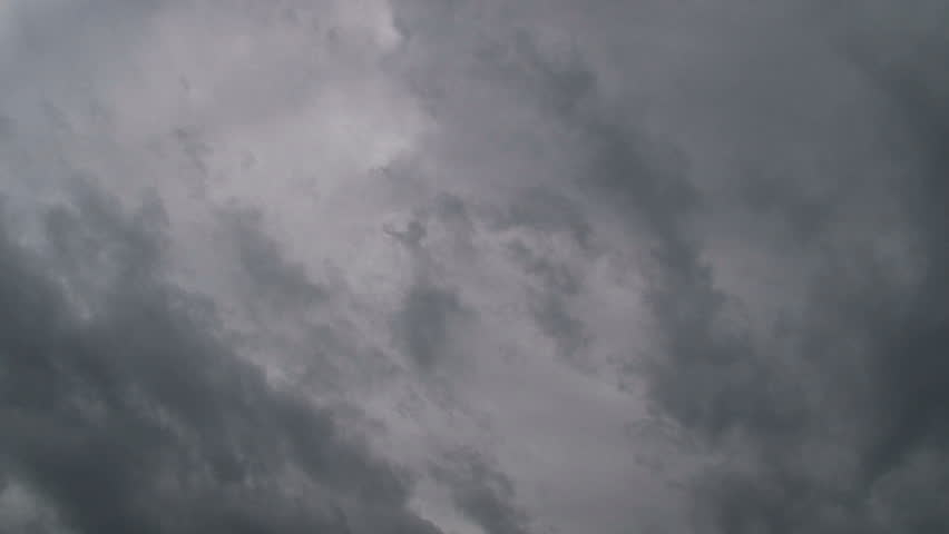 Time lapse of storm clouds moving fast on overcast day with sun peaking through.