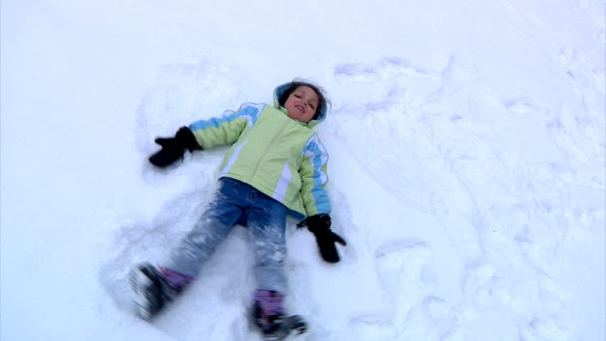 A little girl makes snow angels in the snow.