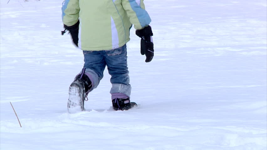 A little girl runs away from the camera in the snow.  Slow motion.