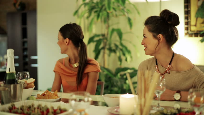 Women sitting at dinner and man bringing punch.
