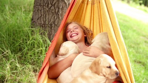 Laughing girl swinging in hammock with puppies in slow motion