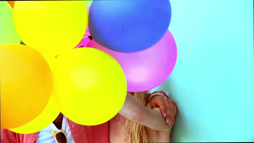 Portrait of happy couple with balloons against turquoise background in slow motion