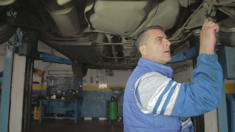 Auto mechanic repairing a car ( under a car lifts) with wrench- dolly