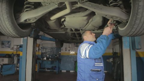 Auto mechanic repairing a car ( under a car lifts) with wrench - dolly