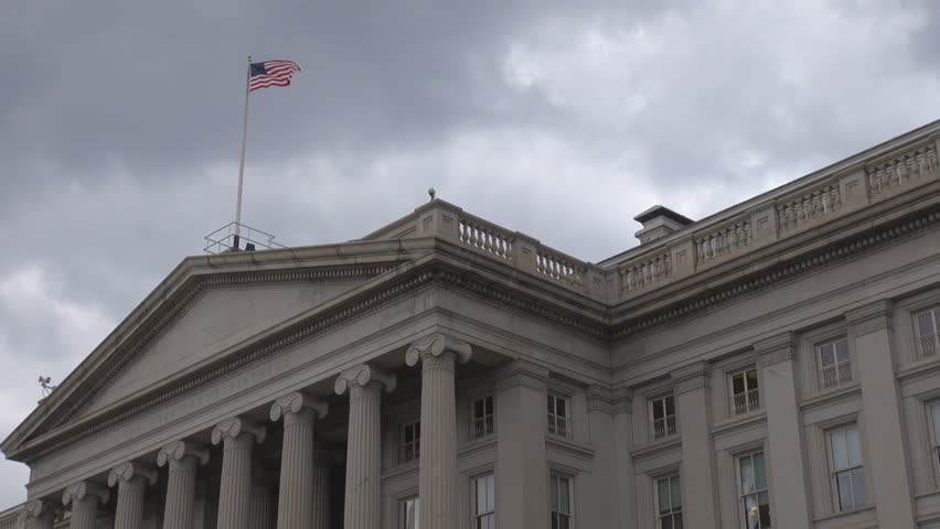 The United States Treasury Department building, the facade with flag and cloudy sky by day in Washington DC, USA