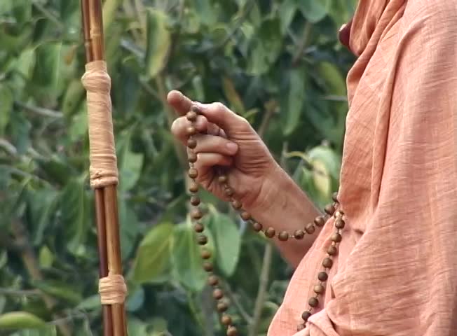 An Indian ascetic chanting on sacred beads against a forest background.