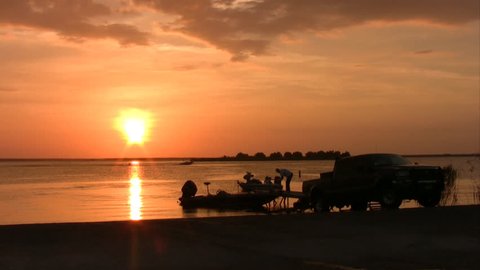 Video of a fishing boat at Chock Canyon Lake in south Texas.  Vivid bright orange sunset. Water ski. Boat being pulled out on boat dock and ramp.