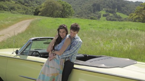 Young couple leaning on a vintage convertible and hugging each other in nature