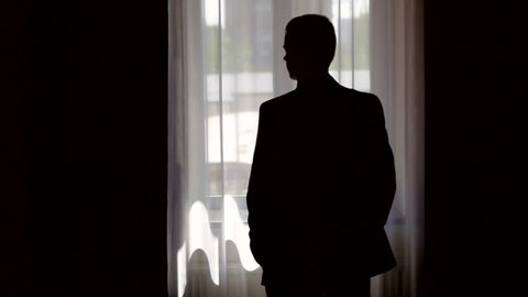 silhouette of stylish man in suit looking out the window, stay home
