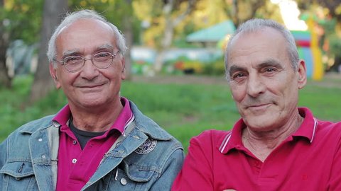 Old men enjoys sitting on a bench in park. Smiling and looking at camera
