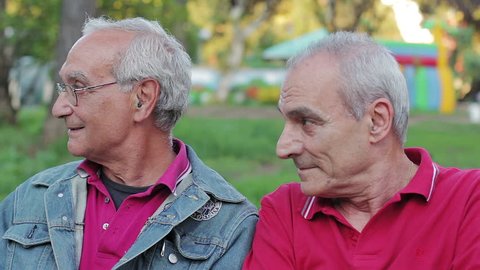 Old men enjoys sitting on a bench in park. Smiling and looking at camera