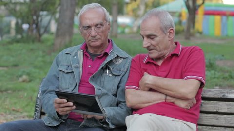 Old man teaching his elderly friends to use a new tablet PC in a park of Rome