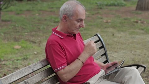 Friendly handsome old man with tablet computer in park