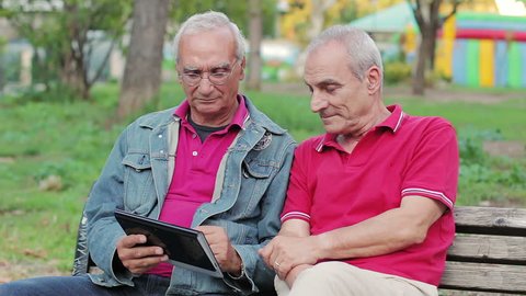 Old man teaching his elderly friends to use a new tablet PC in a park of Rome