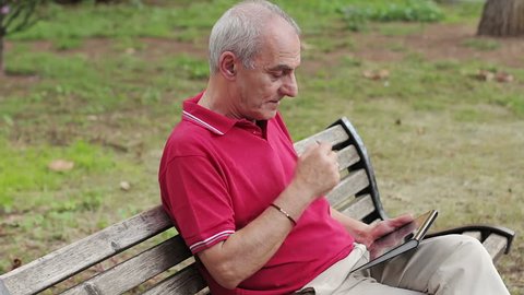 Retired senior man resting and using his tablet at table in park