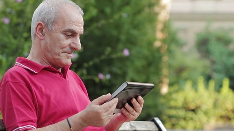 Friendly handsome old man with tablet computer in park