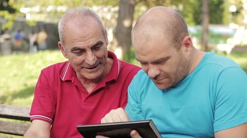 A man and an old man with tablet computer in the park OF Rome