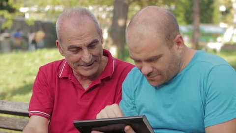 A man and an old man with tablet computer in the park OF Rome