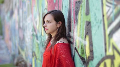 sad woman with a red shirt is crying leaning against a wall painted with murals
