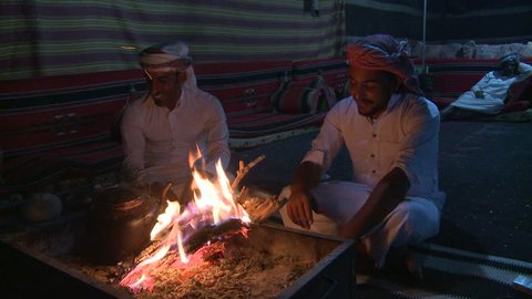 WADI RUM, JORDAN CIRCA 2013 - Two Bedouin men sit in a tent in front of a campfire in the desert and laugh and talk.