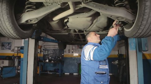 Auto mechanic repairing a car with wrench ( under a car lifts) - dolly