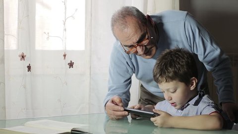 grandfather is learning from his grandson how to use a tablet to surf in web