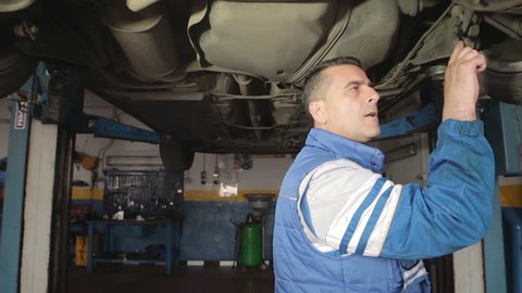 Auto mechanic repairing a car ( under a car lifts) with wrench- dolly