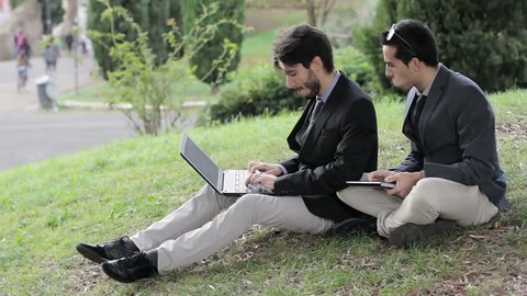 Two business people with tablet and laptop talk about a project on a park