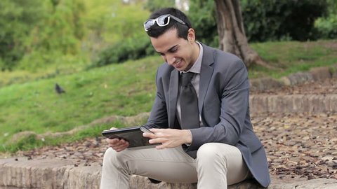 Businessman at the park with tablet sitting on a bench
