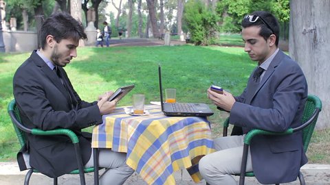 Two businessmen looking at tablet and laptop during business breakfast