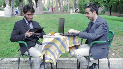 Two businessmen using tablet and laptop during an informal meeting in a bar