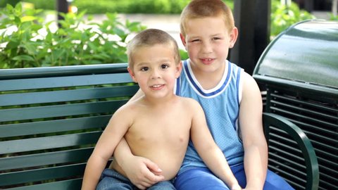 Little and big brother playing on park bench