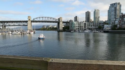 A False Creek Ferry heads towards the historic Burrard Street Bridge. The apartments of the West End neighborhood are in the background. Vancouver, British Columbia, Canada. Dolly shot.