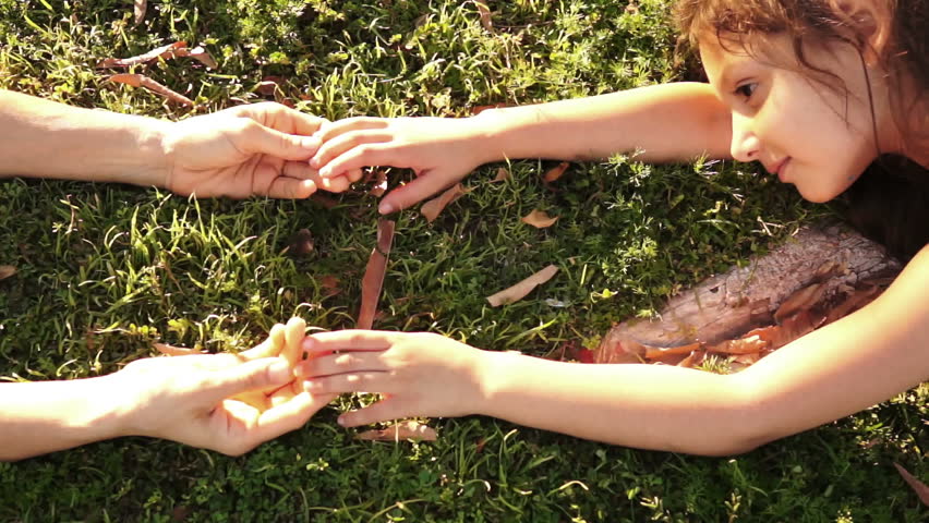 Overhead, dolly shot of a little girl and her mom at a park laying on the grass an playing with each others hands on a sunny day.