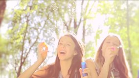 Beauty teen girls having fun outdoors. Beautiful joyful teenagers laughing and blowing soap bubbles in spring park. Girlfriends outdoor. Slow motion video footage 1080p full hd. High speed camera shot