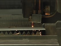 An industrial laser beam cuts  sheet metal on a factory line. A second shot in the clip shows the underside, as sparks fly from the cut metal. Includes audio.