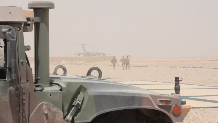 humvee in foreground silhouettes three us marines walking across desert airbase in middle east