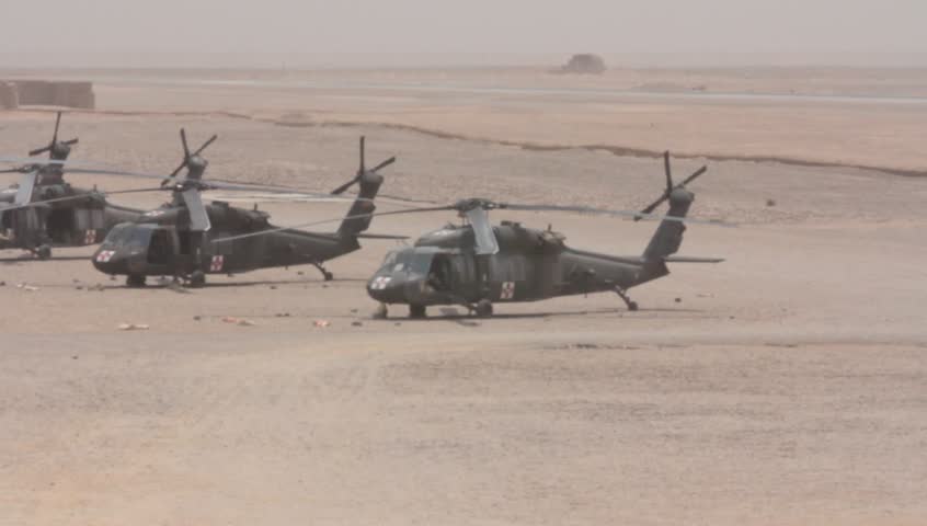 pan shot of huey and apache helicopters in rows at base in middle east