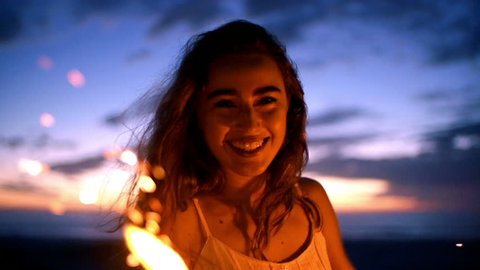 Smiling young woman with sparkler at sunset in slow motionの動画素材